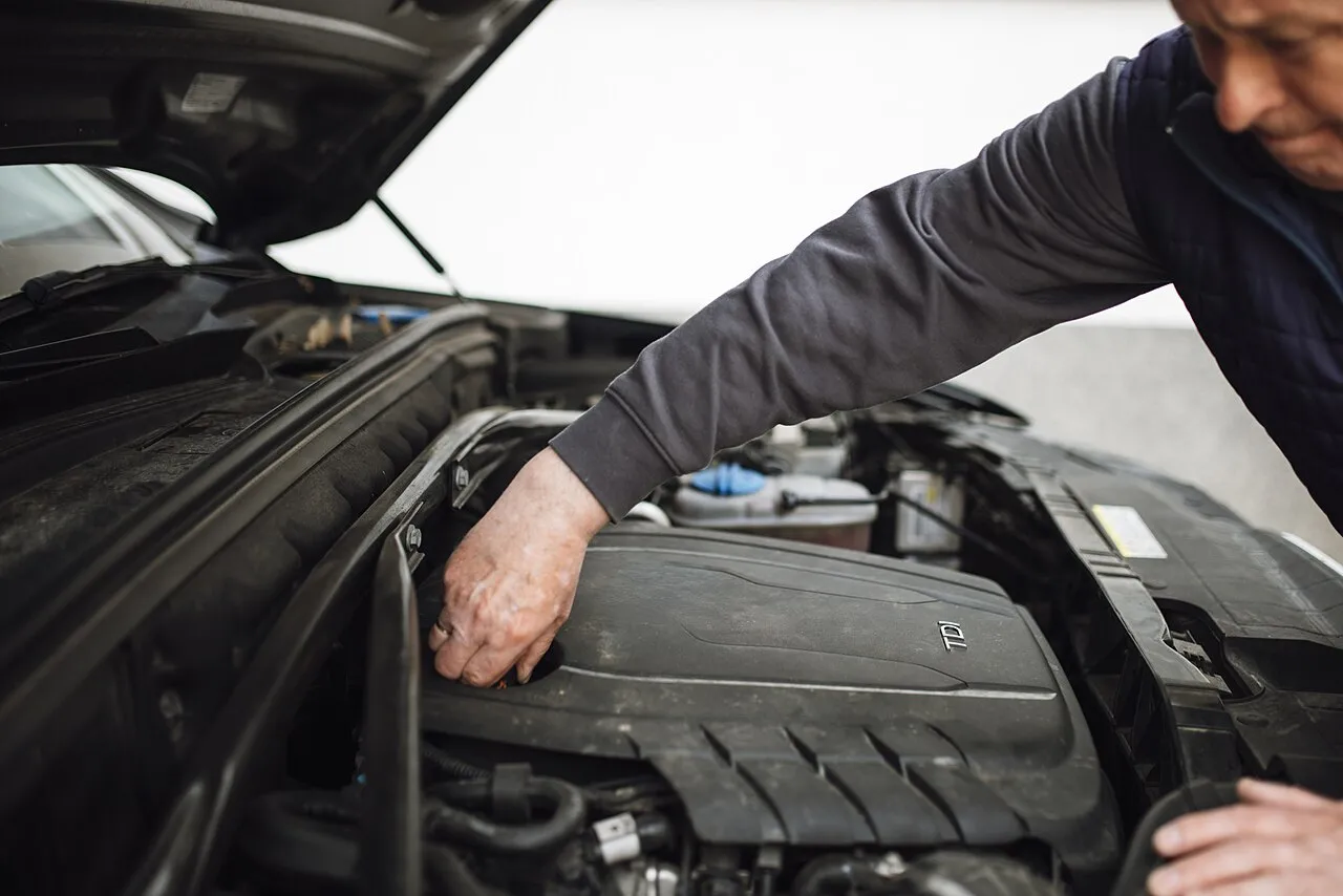 Bir otomobilin motor kaputu altında onarım ve kontrol yapan teknisyen; özel serviste ayıplı hizmet rehberi