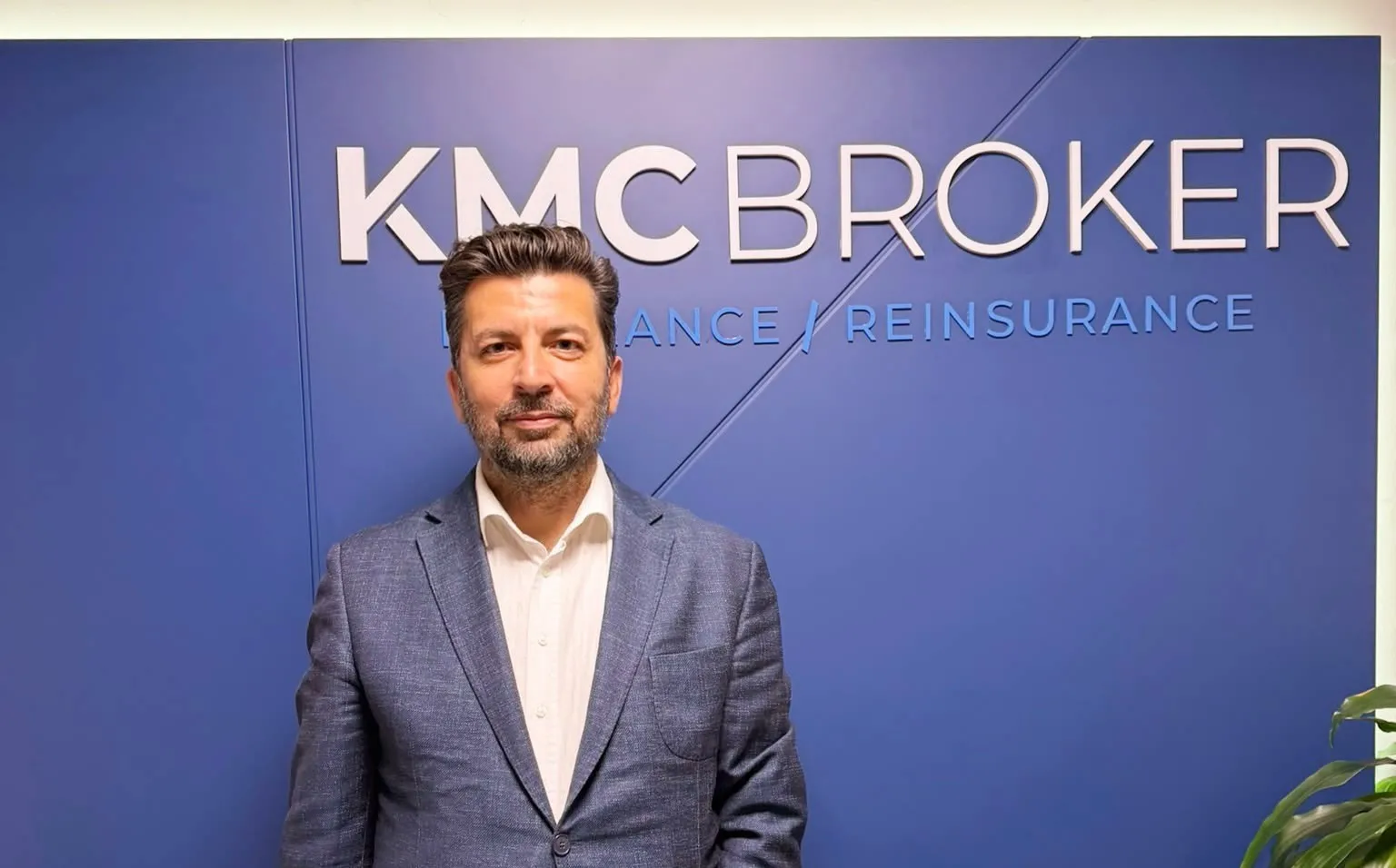 Ali Gülcan, KMC Broker ofisinde şirket logosunun önünde