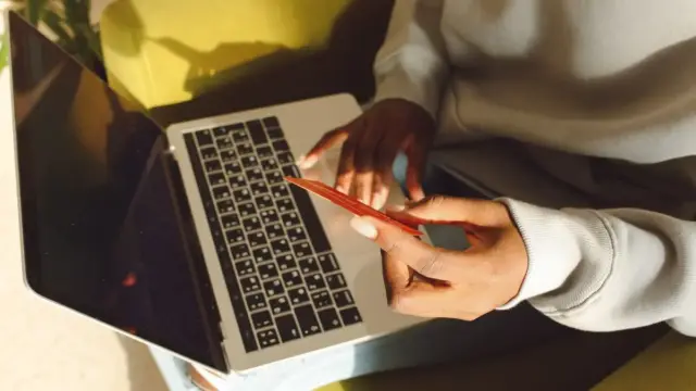 Dizüstü bilgisayarda çevrim içi işlem yaparken kredi kartı tutan kişinin gerçek fotoğrafı; Slingshot Insurance gömülü sigorta altyapısı yatırımı haberi için temsili görsel