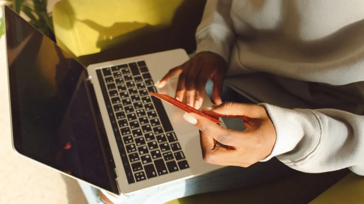 Dizüstü bilgisayarda çevrim içi işlem yaparken kredi kartı tutan kişinin gerçek fotoğrafı; Slingshot Insurance gömülü sigorta altyapısı yatırımı haberi için temsili görsel