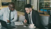 İki iş insanının bilgisayar ve finansal grafikler üzerinden birlikte risk değerlendirmesi yaptığı toplantı