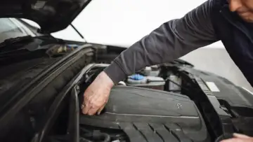 Bir otomobilin motor kaputu altında onarım ve kontrol yapan teknisyen; özel serviste ayıplı hizmet rehberi