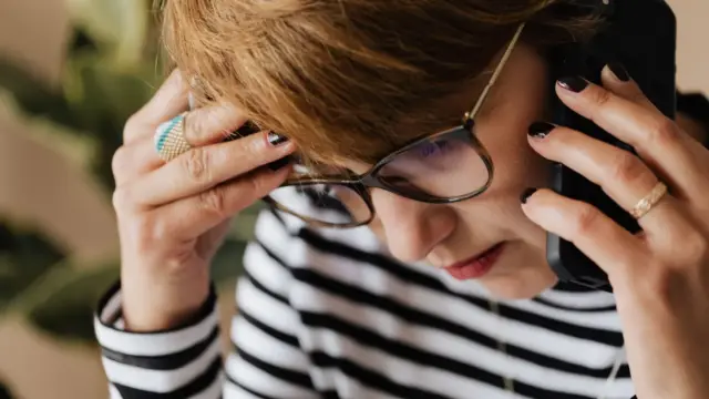 Ofiste telefon görüşmesi sırasında endişeli görünen gözlüklü kadın; ses taklidi dolandırıcılığında şüpheli aramaların doğrulanması rehberini temsil eden gerçek fotoğraf