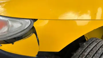 Sarı bir otomobilin darbe ve çizik bulunan ön tamponu ile farı; park yerinde çarpıp kaçma ve Güvence Hesabı konulu rehber için temsili gerçek araç hasarı fotoğrafı