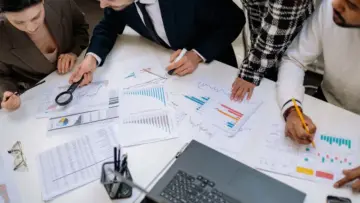 Ofiste finansal grafikler ve raporlar üzerinde çalışan profesyoneller; ARC'nin banka ve varlık yöneticileri için kredi portföyü ödeme yapmama sigortasını temsil eden gerçek fotoğraf