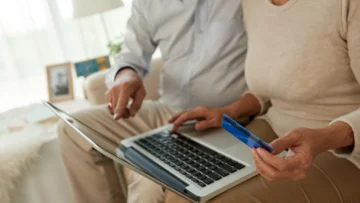 Evde dizüstü bilgisayar üzerinden banka kartıyla çevrim içi işlem yapan iki kişi