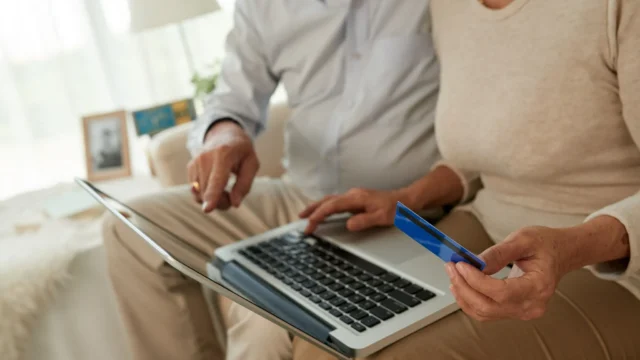 Evde dizüstü bilgisayar üzerinden banka kartıyla çevrim içi işlem yapan iki kişi