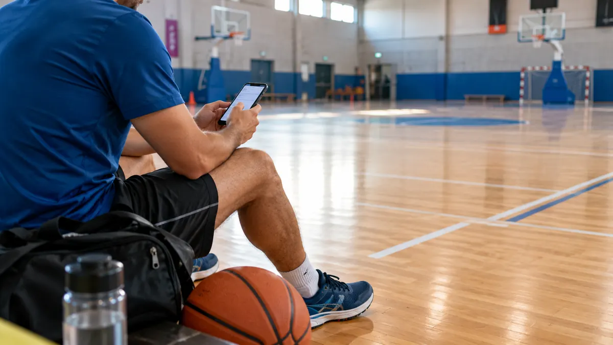 Spor salonunda basketbol topu ve antrenman çantası yanında telefonuyla işlem yapan sporcu